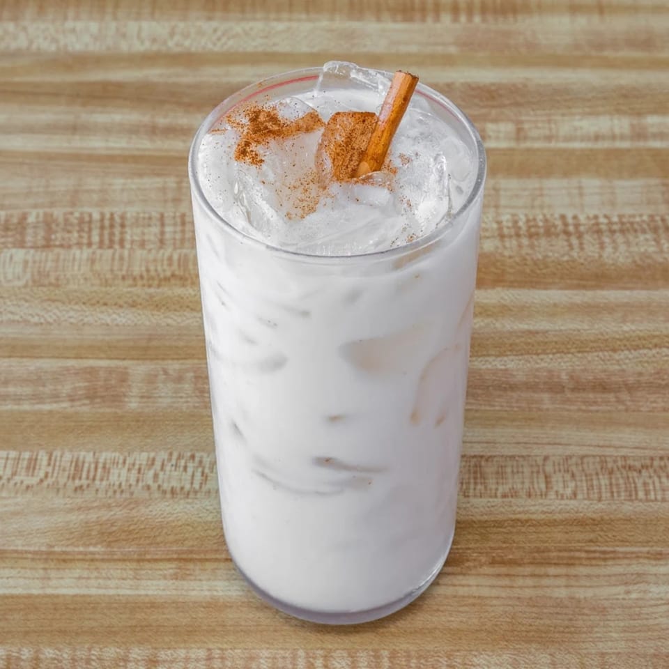 Horchata drink with ice, cinnamon stick, and cinnamon powder on a wooden table.