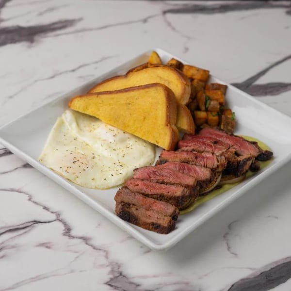 Steak and eggs breakfast with sliced steak, scrambled eggs, toast, and roasted potatoes on a white plate.