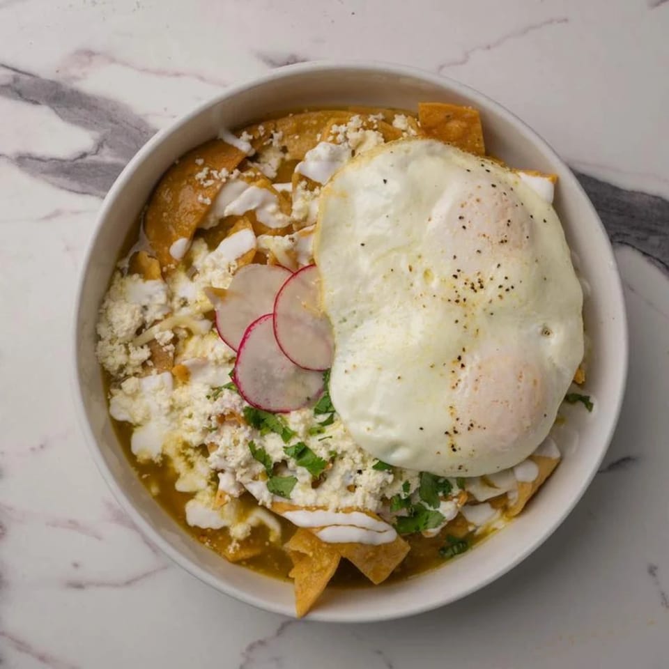 Chilaquiles with green sauce, topped with two fried eggs, crumbled cheese, radishes, and cilantro.