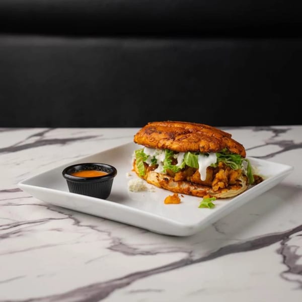 A Mexican torta sandwich with meat, lettuce, and white sauce, served with a side of orange sauce.