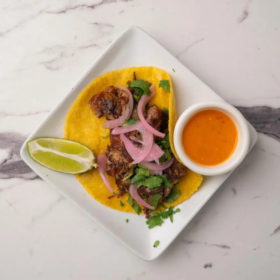 A single carnitas taco with pickled red onions, cilantro, lime, and a side of orange sauce.